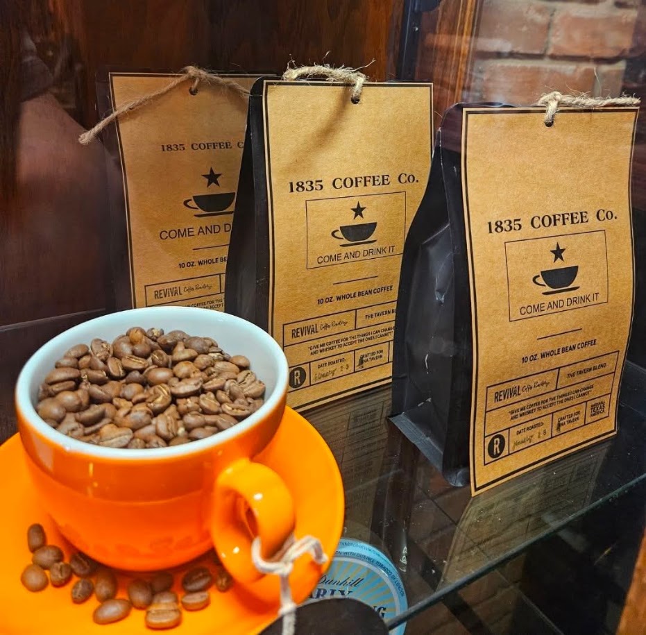 Bags of 1835 Coffee Co. whole bean coffee with a cup of roasted beans