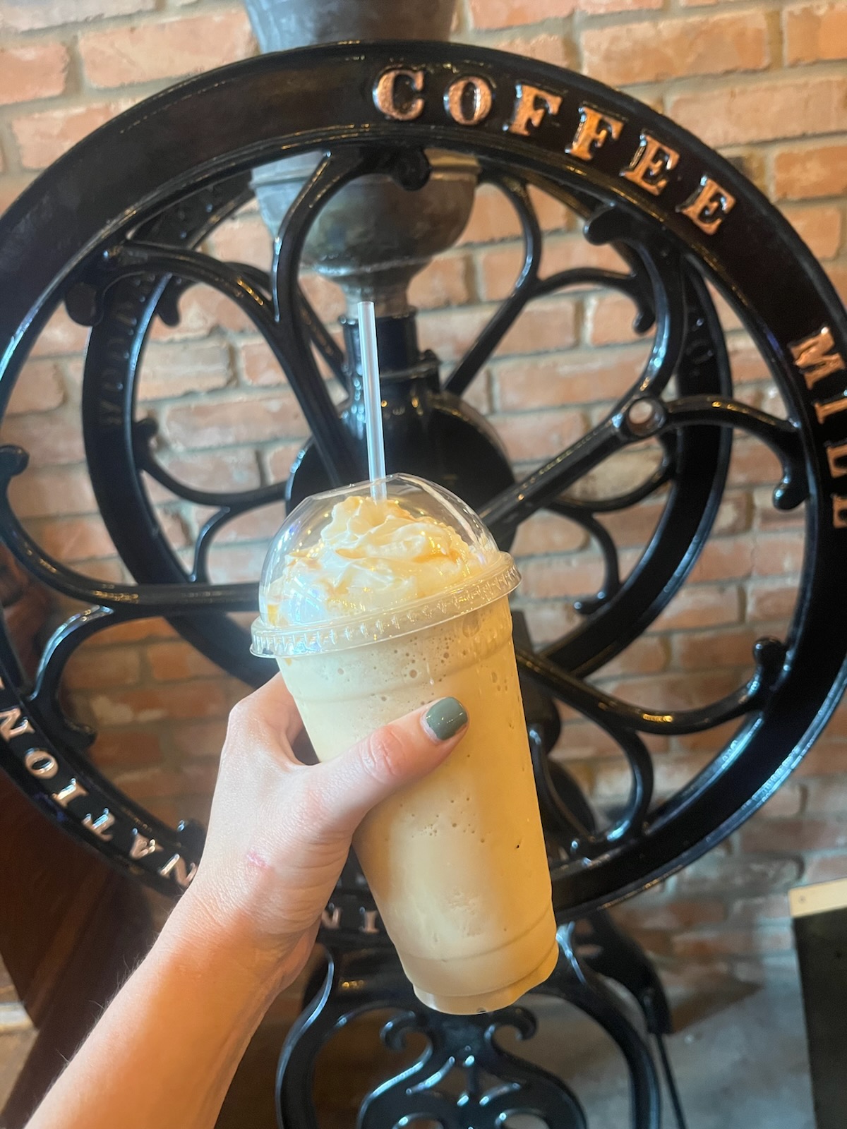 Iced coffee held in front of an antique cast-iron coffee mill at 1835 Coffee Company