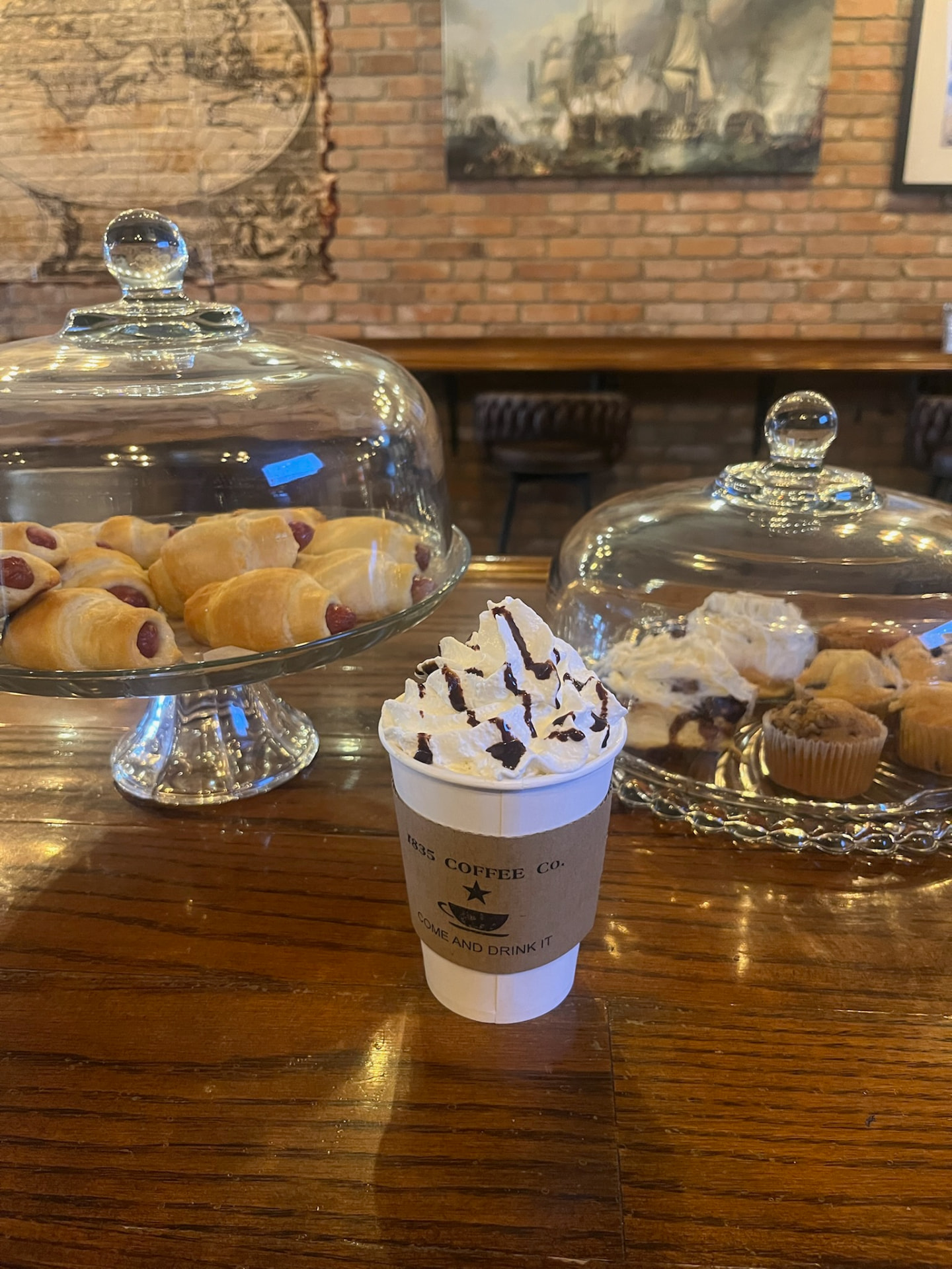 Whipped-cream topped 1835 Coffee Co. drink beside kolaches and muffins on the counter