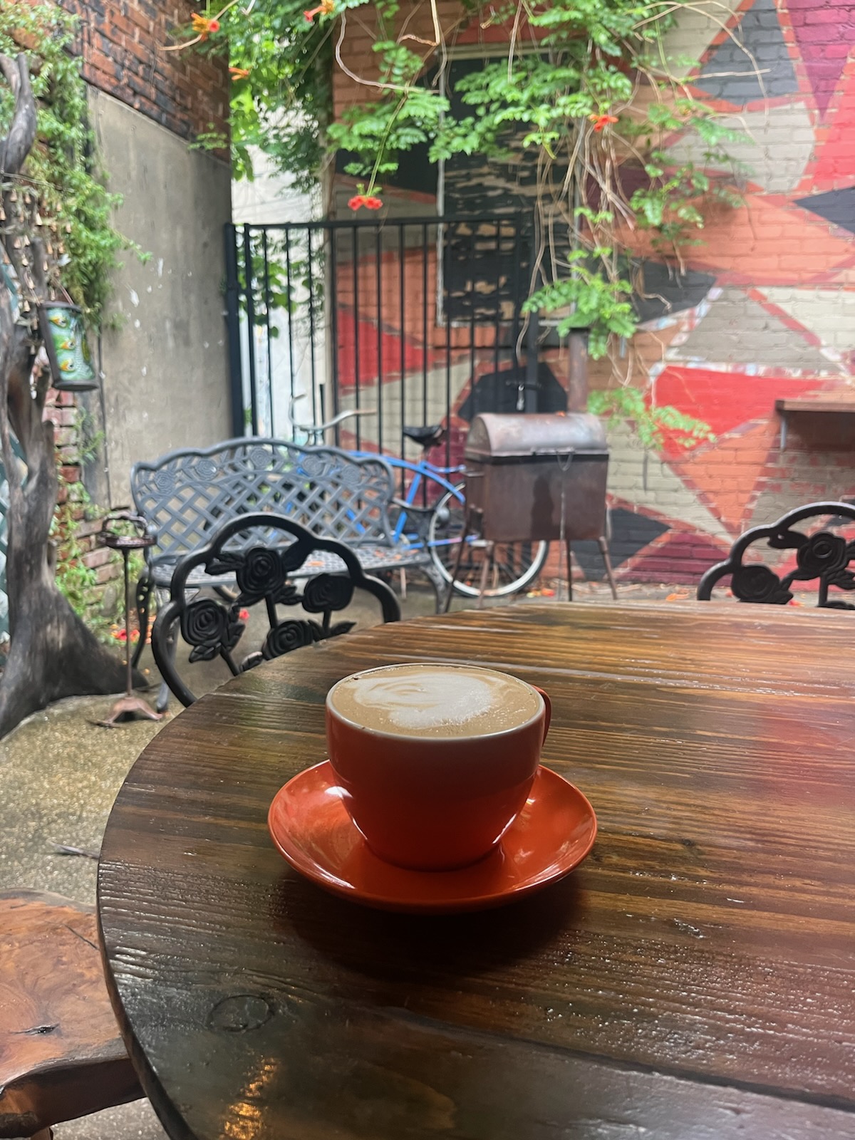 Latte in a red cup on a wooden table on the outdoor patio with mural wall